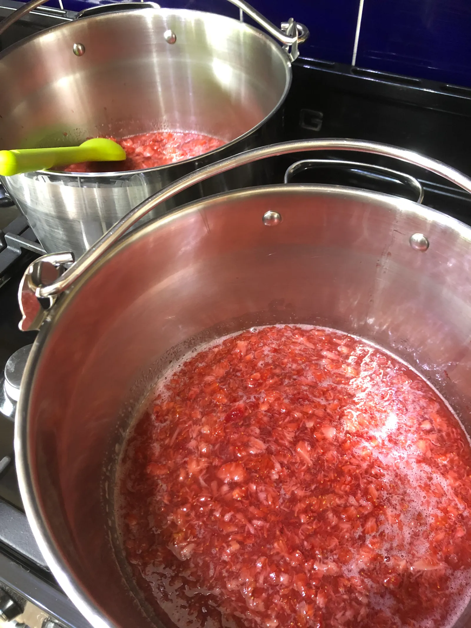 Two large pans of strawberry jam coming up to a rolling boil on Sarah’s range cooker.